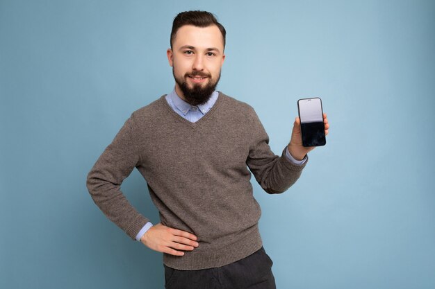 Guapo feliz fresco joven morena sin afeitar con barba vistiendo elegante suéter gris y azul