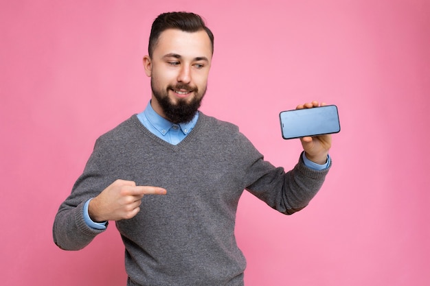 Guapo feliz fresco joven morena sin afeitar con barba vistiendo elegante suéter gris y azul