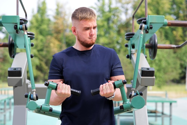 Guapo feliz hombre fuerte atleta culturista entrenamiento al aire libre en la máquina de gimnasio en verano ganar manos