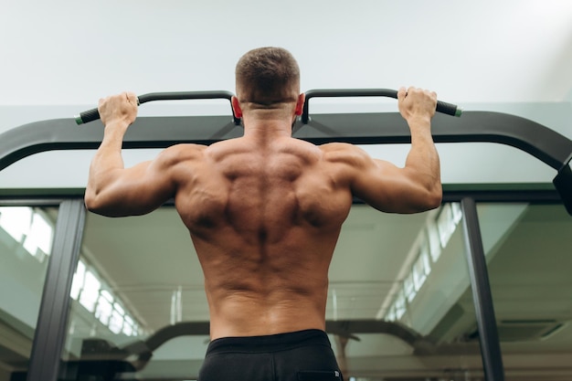 Guapo fitness hombre haciendo ejercicios de espalda con barra horizontal en el gimnasio vista trasera joven atleta haciendo pull ups