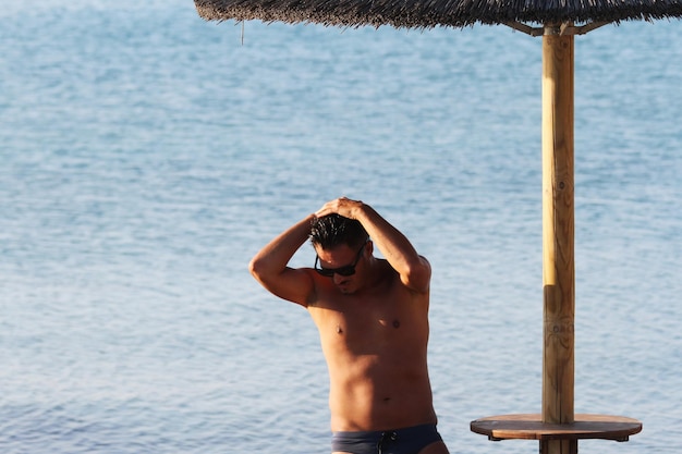 Guapo con gafas de sol y traje de baño están disfrutando en la playa al atardecer Apulia Salento Italia