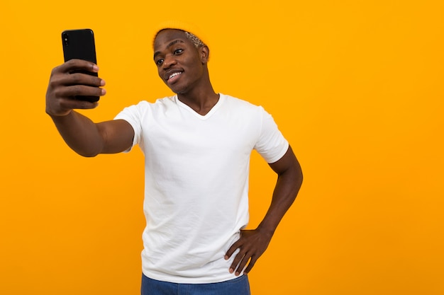 Guapo hombre africano negro hace selfie en el teléfono en naranja con espacio de copia