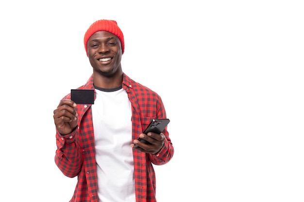 Guapo hombre americano de piel oscura vestido con una camisa roja y una gorra anuncia una tarjeta y un