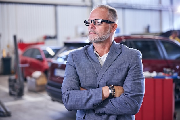 Guapo hombre barbudo de pie en el taller de reparación de automóviles