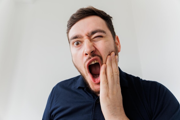 Guapo hombre barbudo que sufre de dolor de muelas tocando su mejilla para detener el dolor contra el blanco