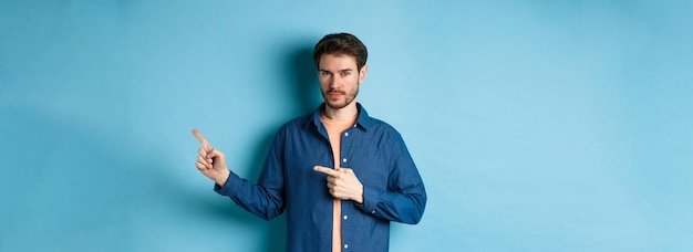 Guapo hombre barbudo señalando con el dedo los derechos en el espacio vacío y mirando confiado de pie en azul b