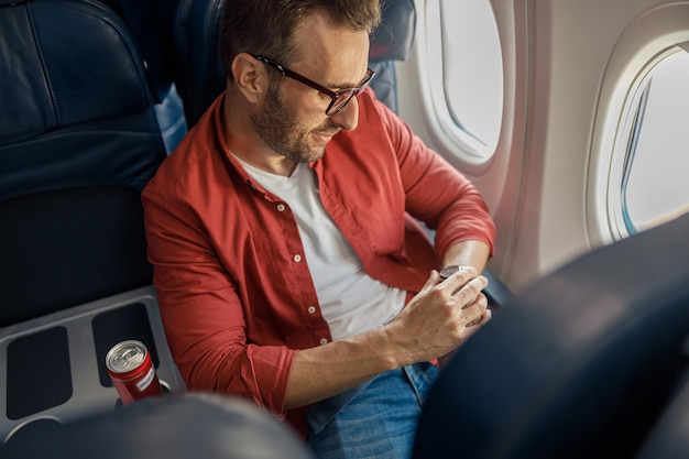 Guapo hombre caucásico en ropa casual y gafas comprobando la hora de llegada en su reloj sentado en el