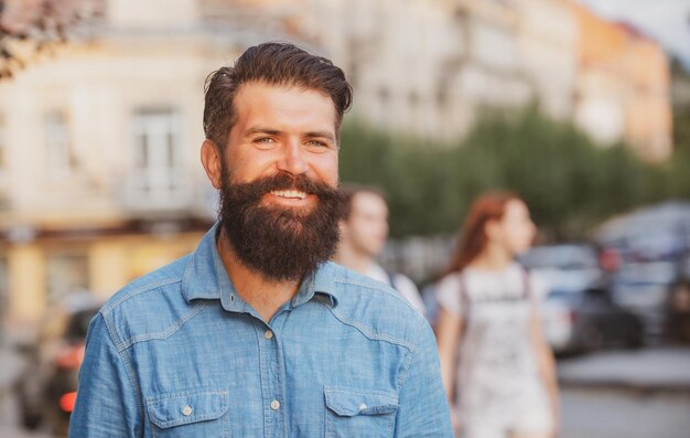 Guapo hombre elegante sonriente vestido con ropa de chaqueta de jeans Hombre de moda urbana posando en el fondo de la calle
