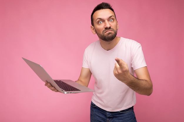 Guapo hombre enojado e iracundo con ordenador portátil mostrando el dedo mirando a cámara en camiseta