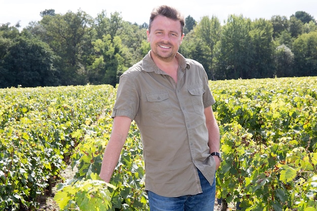 Guapo hombre feliz sonriendo a la cámara en los campos de uva