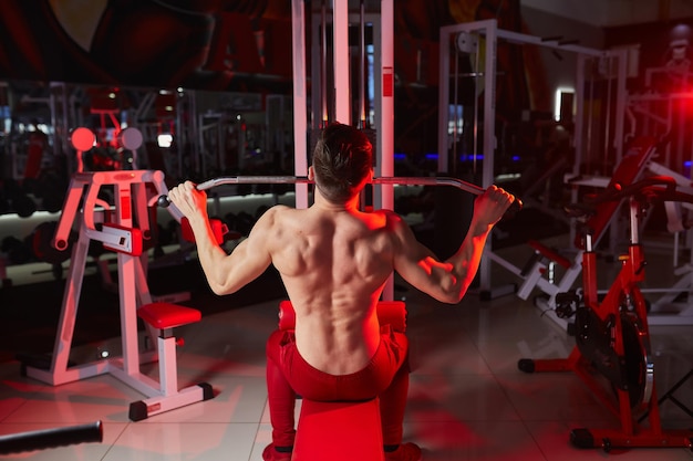 Guapo hombre fitness haciendo ejercicio de peso pesado para la espalda en la máquina