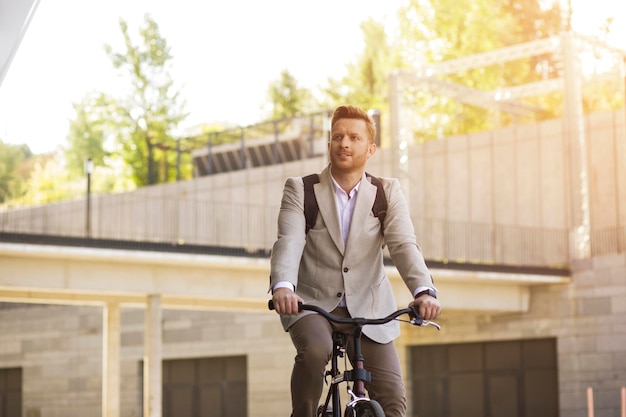 Guapo hombre formalmente adecuado conduciendo su bicicleta en la calle y mirando hacia otro lado