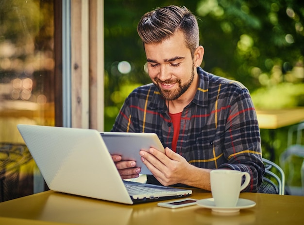 Guapo hombre hipster barbudo usando una computadora portátil en un café.