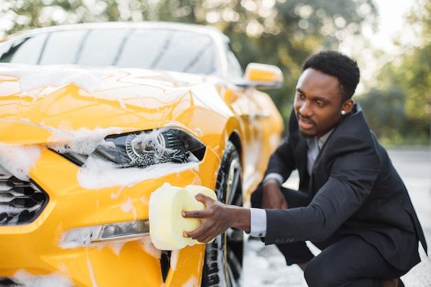 Guapo hombre de negocios con estilo africano barbudo limpiando su coche amarillo de lujo