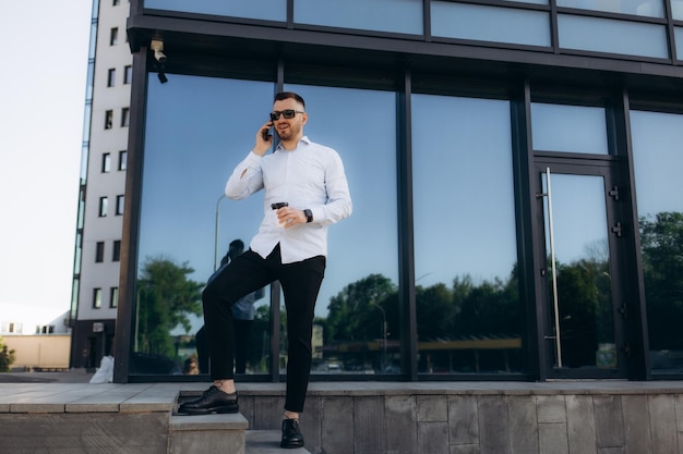 Foto guapo hombre de negocios moderno hipster con barba caminando por la ciudad y llamando por teléfono móvil