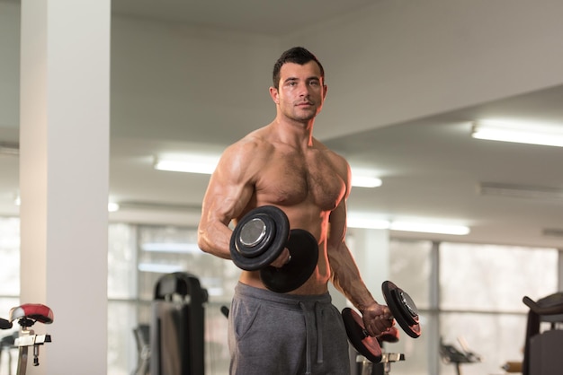 Guapo hombre peludo trabajando bíceps en un gimnasio rizos de concentración de mancuernas de gimnasio