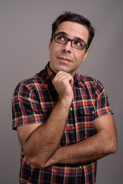 Guapo hombre persa con anteojos contra la pared gris