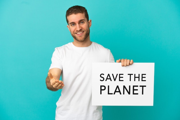 Guapo hombre rubio sobre fondo azul aislado sosteniendo un cartel con el texto Save the Planet haciendo un trato