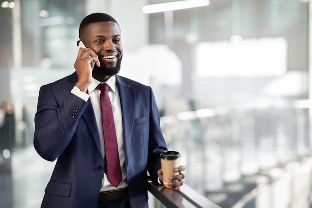 Foto guapo jefe negro teniendo conversación telefónica bebiendo café