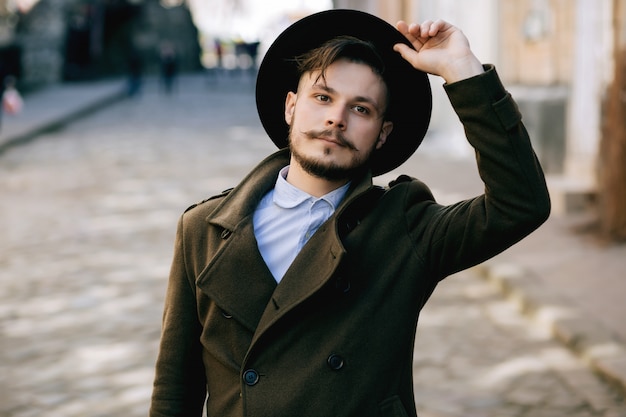 Guapo joven barbudo hipster hombre chico con sombrero en la calle con maleta.