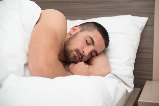 Guapo joven estudiante masculino durmiendo felizmente en la cama blanca