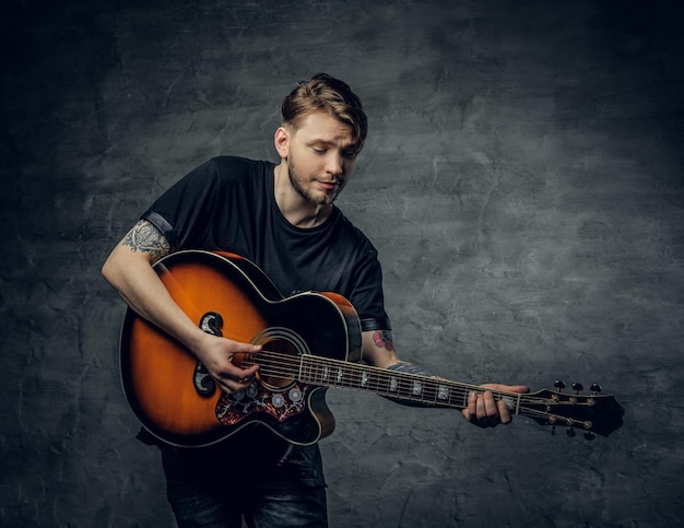 Guapo joven jugador de blues de guitarra acústica con tatuajes en los brazos realizando sus habilidades musicales.