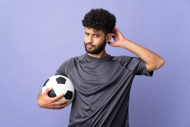 Guapo joven jugador de fútbol marroquí hombre sobre aislado en la pared púrpura con dudas