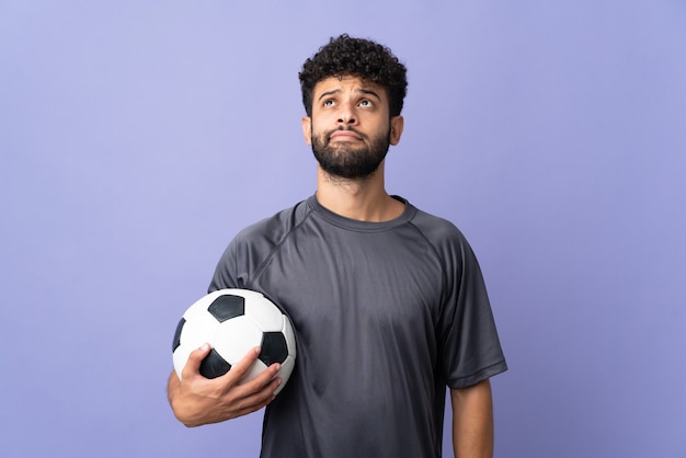 Guapo joven jugador de fútbol marroquí hombre sobre aislado en la pared púrpura y mirando hacia arriba