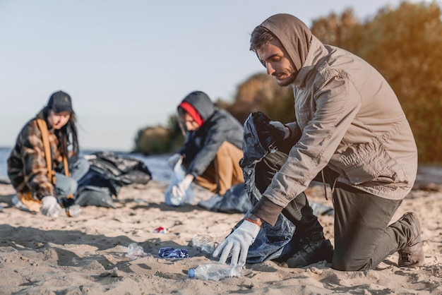 Guapo joven voluntario con equipo recogiendo basura en la orilla del mar