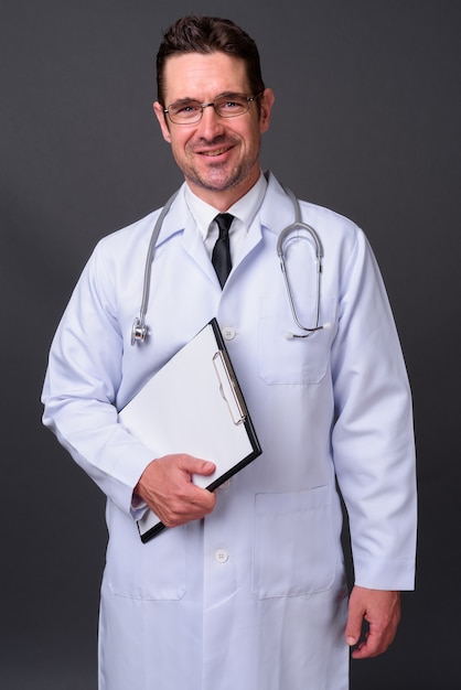 Guapo médico barbudo con anteojos contra la pared gris