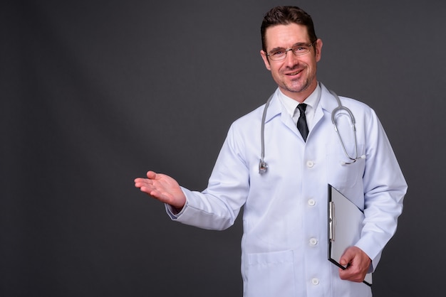 Guapo médico barbudo con anteojos contra la pared gris