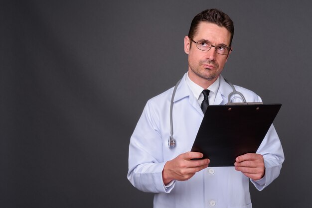 Guapo médico barbudo con anteojos contra la pared gris