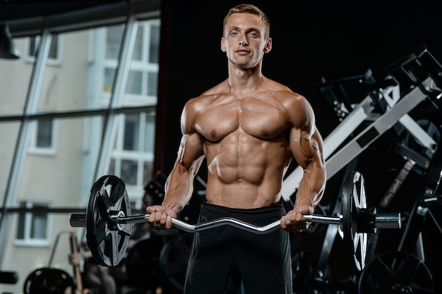 Guapo modelo joven entrenamiento brazos en gimnasio