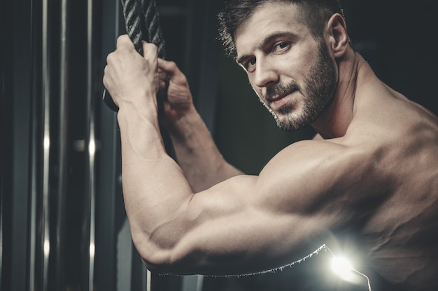 Guapo modelo joven entrenamiento brazos en gimnasio