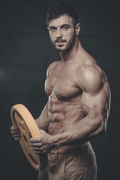 Foto guapo modelo joven entrenamiento brazos en gimnasio