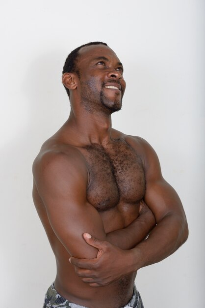 Guapo musculoso hombre africano barbudo sin camisa contra la pared blanca