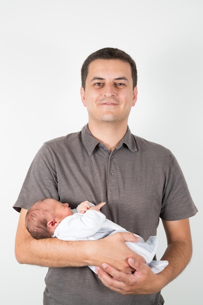 Guapo padre con bebé recién nacido en brazos posando en fondo blanco.