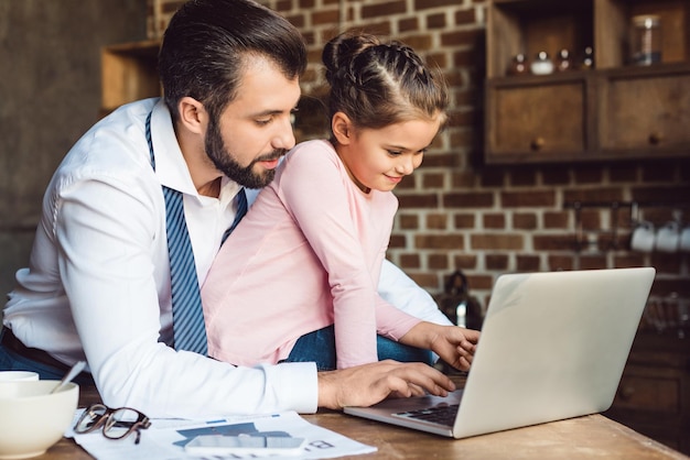 Guapo padre e hija usando laptop juntos en la cocina