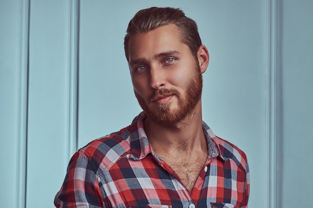 Un guapo pelirrojo con estilo en una camisa de franela, posando en un estudio contra una pared blanca.