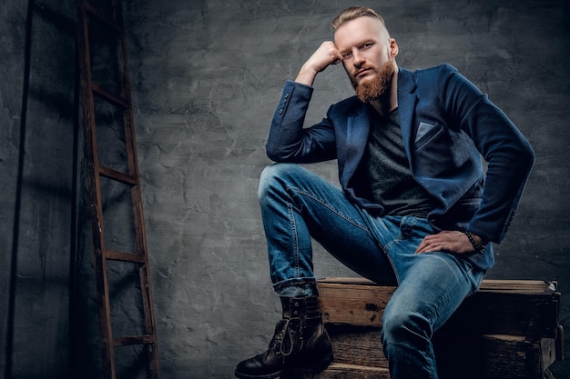 Un guapo pelirrojo vestido con jeans y una camisa posando en una caja de madera.