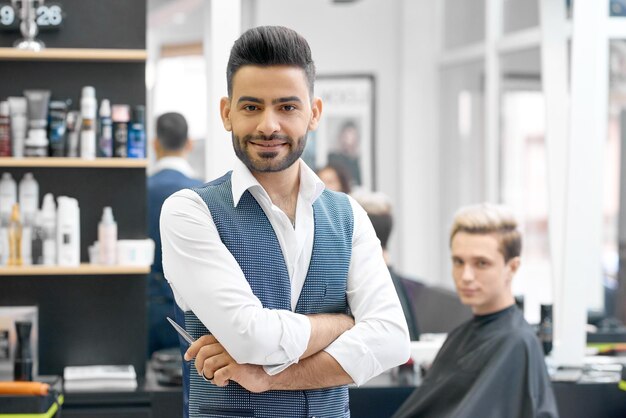 Guapo peluquero posando de pie frente a un joven cliente sentado cerca del espejo