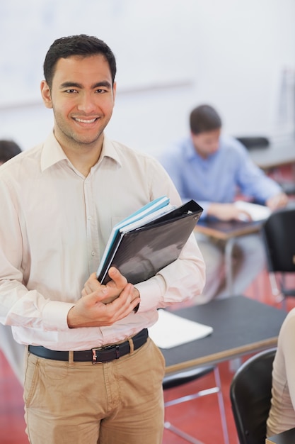 Guapo profesor de pelo negro posando en su clase con algunos archivos