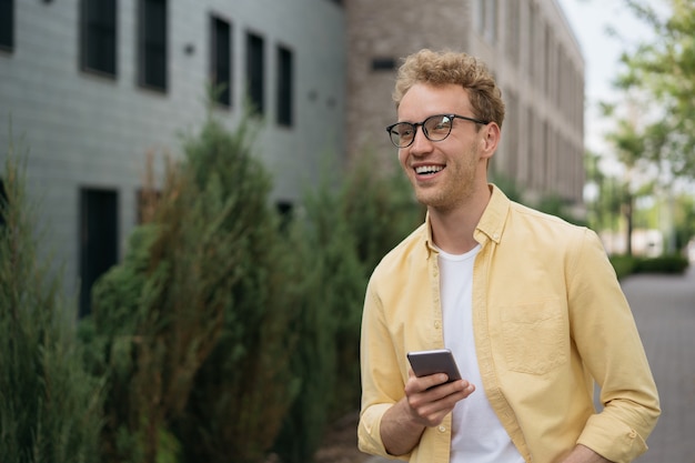 guapo, sonriente, hombre, utilizar, teléfono móvil, esperar, taxi, aire libre