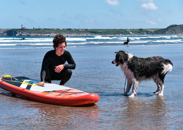 Guapo surfista de pelo largo y rizado con un aspecto encantador en su perro border collie