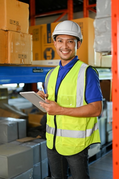 Guapo trabajador de almacén asiático sonriendo mirando a la cámara mientras trabaja en el almacén