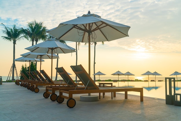 guarda-chuva com piscina ao redor da piscina com fundo do mar oceano ao pôr do sol ou nascer do sol - conceito de férias e férias