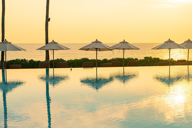 Guarda-chuva com piscina de cama ao redor da piscina com fundo do mar oceano ao pôr do sol ou nascer do sol - conceito de férias e férias