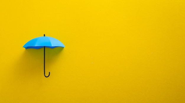 Guarda-chuva de brinquedo azul no conceito de cobertura de seguro de fundo amarelo