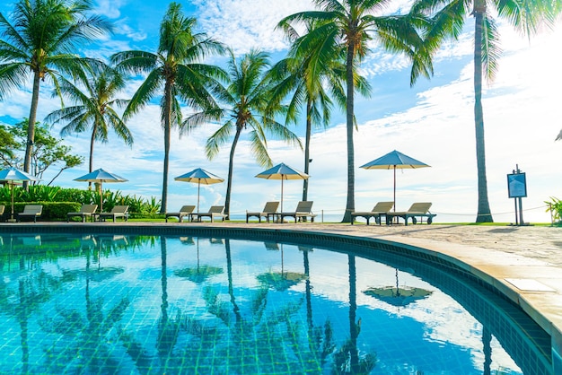 Guarda-chuva de luxo e cadeira ao redor da piscina no hotel e resort com palmeira de coco no céu pôr do sol ou nascer do sol