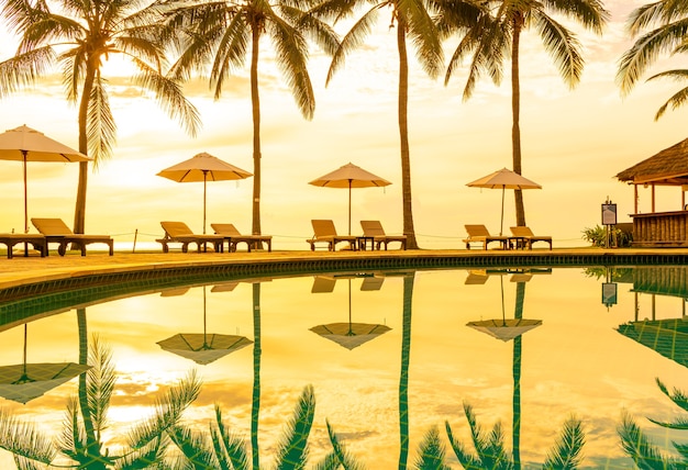 Guarda-chuva e cadeira ao redor da piscina em hotel resort para viagens de lazer e férias perto da praia do mar, oceano, ao pôr do sol ou ao nascer do sol